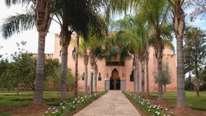 Un chemin menant à un bâtiment orné d’arches et bordé de palmiers.