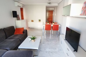 A modern living room with a sofa, coffee table, TV, and dining area with chairs and a table. - Appartment Zephyrus by DENIA COSTA (Dénia)