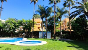 Piscina cercada por palmeiras e um edifício com varandas.