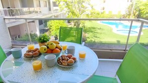 Varanda com mesa posta para o café da manhã, piscina e vista para o verde ao redor.