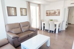 A modern living room with a brown sofa, a white coffee table, and a dining area with white chairs and a table.