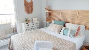A bedroom with a bed, bedside tables, a macrame wall hanging, and a window. - Apartament Victoria Playa by DENIA COSTA (Denia)