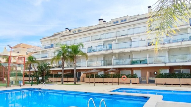 A swimming pool with a clear blue water, surrounded by a building with multiple balconies and a palm tree. - Apartament Victoria Playa by DENIA COSTA (Denia)