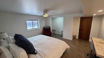 A bedroom with a bed, a desk, a chair, a red chair, a window, and a door.