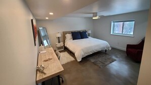 Una camera da letto moderna con un grande letto, una scrivania, una sedia, uno specchio, una ventola a soffitto e una finestra.