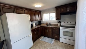 Eine Küche mit dunklen Holzschränken, einem weißen Kühlschrank, einem eingebauten Backofen und einem Fenster über der Spüle.