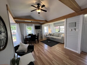 Una sala de estar acogedora con techo de madera, un comedor con mesa y sillas, un sofá y un reloj en la pared.