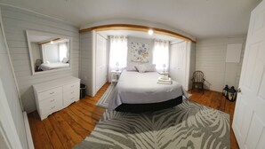 Ein Schlafzimmer mit einem großen Bett, einem Schminktisch, einem Sessel und einem Spiegel.