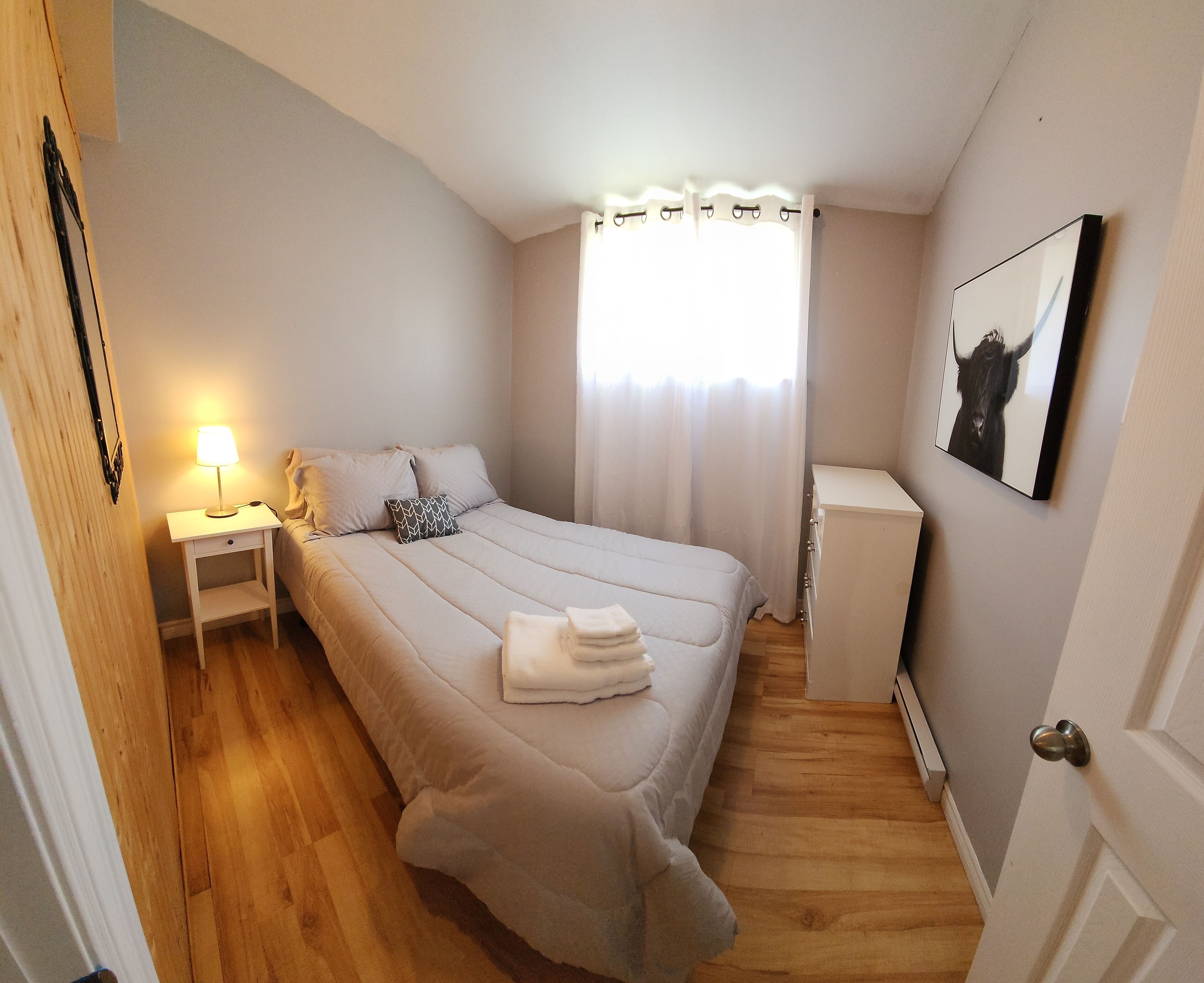A bedroom with a bed, bedside table with a lamp, a dresser, and a framed picture on the wall.