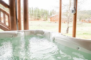 Un bain à remous avec vue sur un chalet en bois et des arbres en arrière-plan.