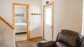 A room with a wooden staircase, a bed with a white headboard, a brown leather chair, and a coat rack with hooks. - Welcome to Goldfinch! (Hill City)