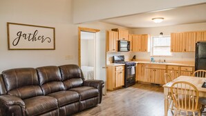 A modern kitchen with wooden cabinets, a dining table, and a leather sofa. - Welcome to Goldfinch! (Hill City)