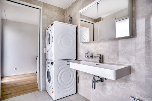 A modern bathroom with a stacked washer and dryer, a large mirror, and a sleek sink.