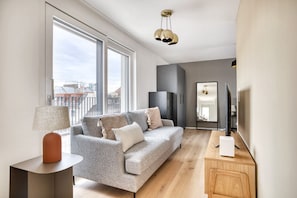 Una sala de estar moderna con un sofá gris, una mesita auxiliar, un espejo y un mueble para televisión.