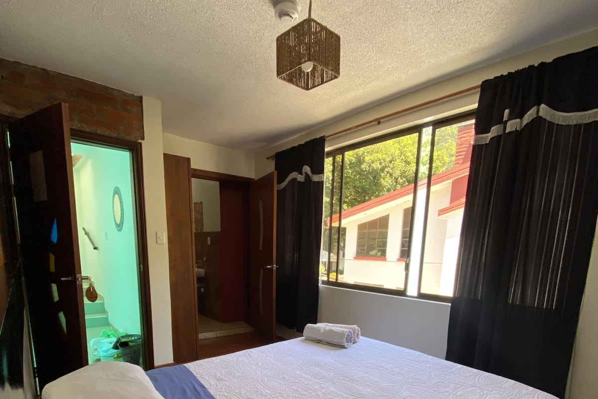 Ein Hotelzimmer mit einem großen Bett, einem Deckenventilator, einem Fenster mit Vorhängen und Blick ins Freie.