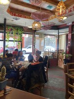Un restaurante con mesas y sillas, adornos colgantes y vista a la calle.