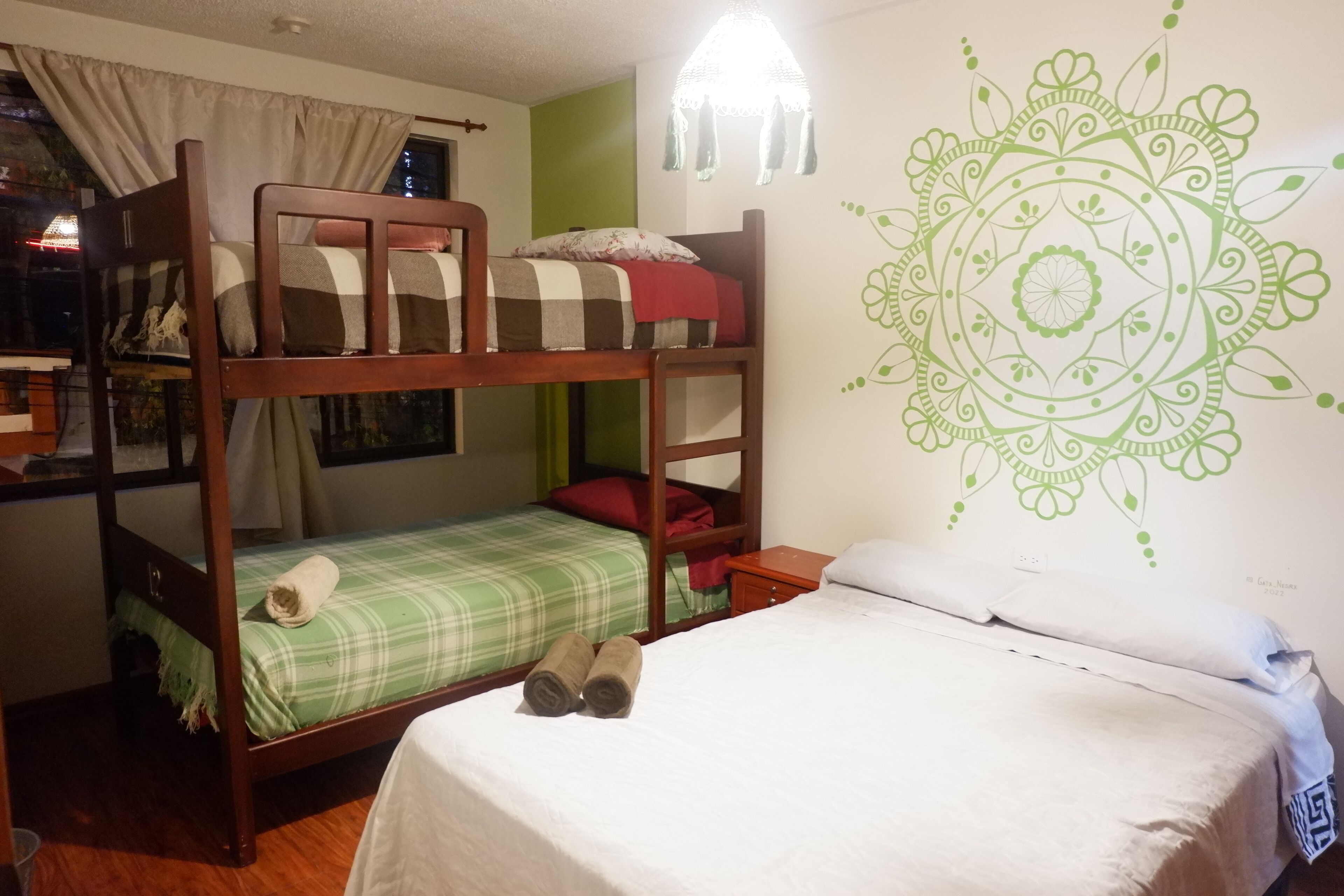 Ein Schlafraum mit Etagenbetten, eine grün-weiß karierte Bettdecke, ein Bett unten und Wandkunst mit einem dekorativen Mandala.