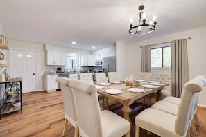Une cuisine moderne avec des meubles blancs, une table à manger en bois pour six personnes et un lustre.