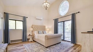 A bedroom with a large bed, a nightstand, a chandelier, and a view of the outdoors through a window.