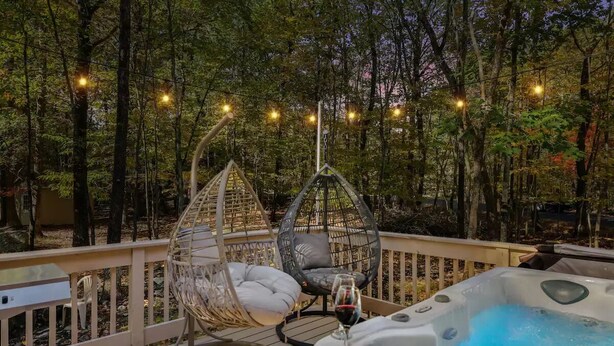 A deck with a hot tub, two hanging chairs, and string lights.