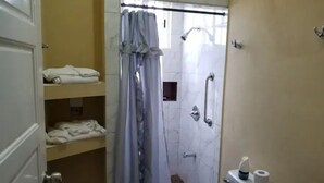 A bathroom with a shower, toilet, and a sink. There are towels on a shelf and a shower curtain. - Royal View Apartment - One bedroom, one bathrooms (Belize City)
