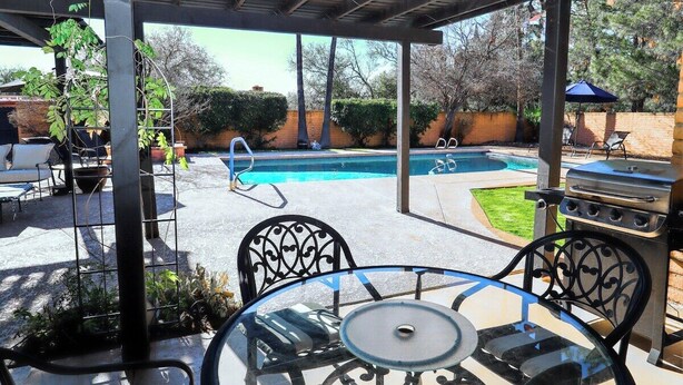 Un área de patio exterior con piscina, una parrilla y una mesa con sillas.