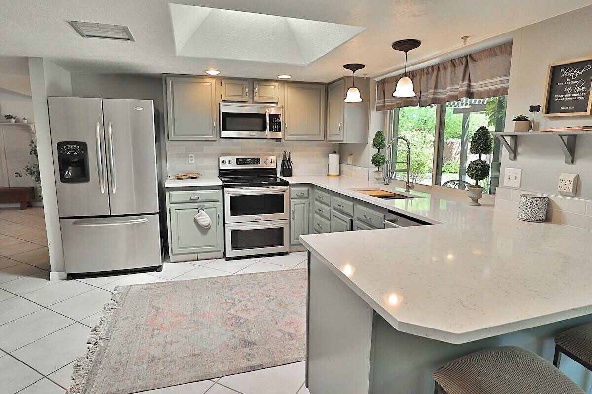 A modern kitchen with a central island, built-in appliances, and a large window providing natural light.