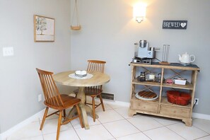 A dining area with a round wooden table, two chairs, a coffee machine, and a shelf with kitchen items. - Sabino Vista Charming Quiet Home with Pool (Tucson)