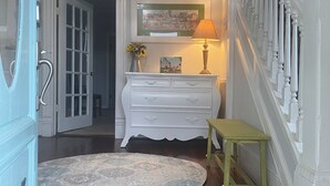 A hallway with a wooden floor, a white dresser with drawers, a small table, a lamp, and a framed picture on the wall. - Adorable 1899 historic “The Butter Bean Lady” storybook home (Columbus)