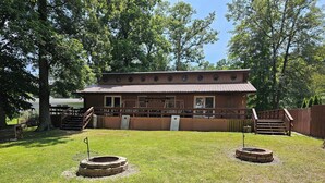 A two-story wooden building with a fenced deck, a fire pit, and a covered outdoor seating area.