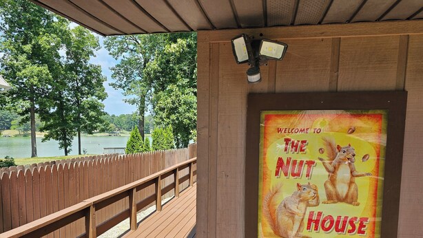A wooden deck with a view of a lake and trees, and a sign reading "Welcome to The Nut House".