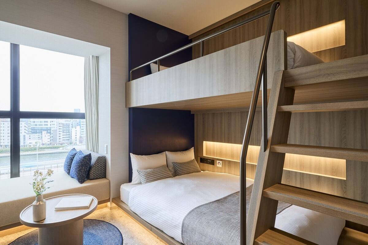 Une chambre d’hôtel moderne avec un lit superposé, un bureau avec une chaise, un vase de fleurs et une vue sur la ville.