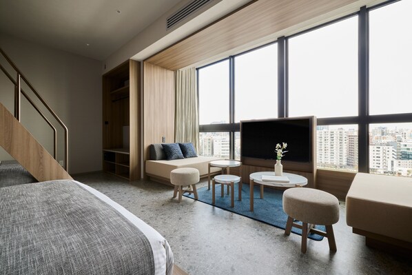 Una camera d'albergo moderna con un letto grande, un divano, una TV e vista sulla città.