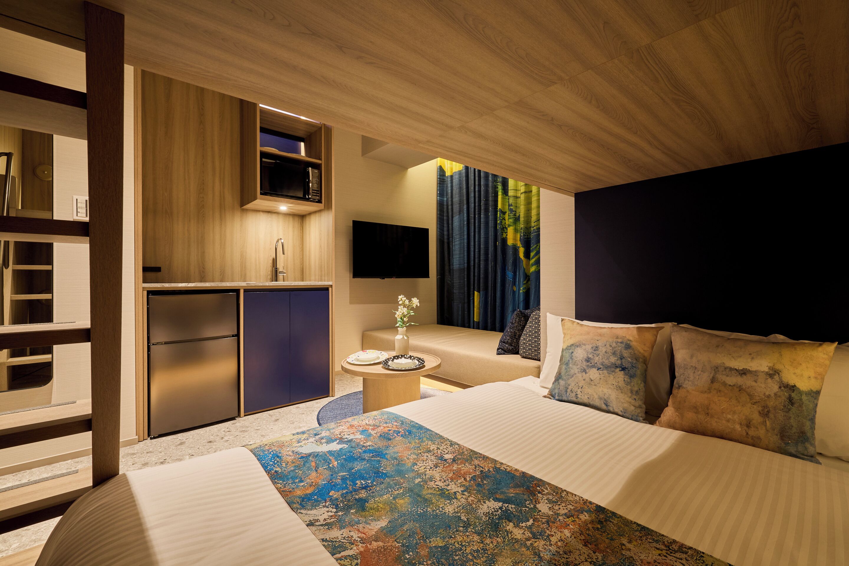 Habitación de hotel moderna con una cama grande, una kitchenette pequeña, un televisor de pantalla plana y vistas al exterior.