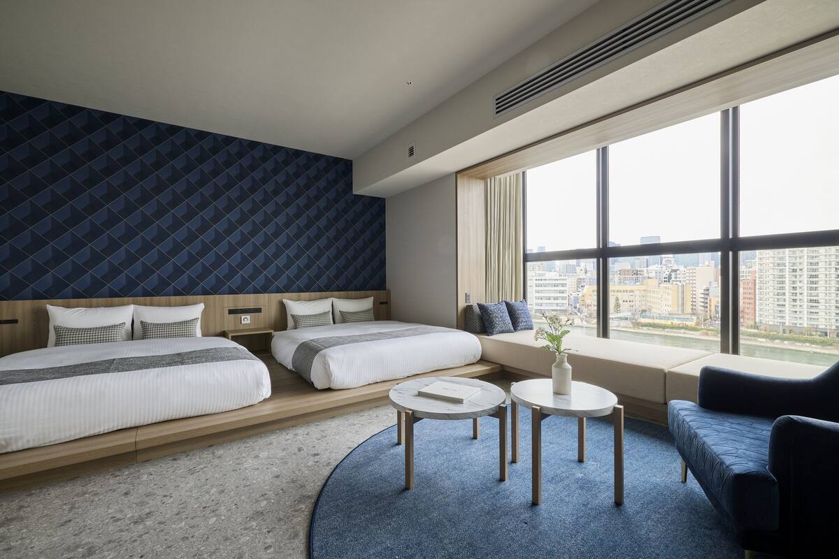 A modern hotel room with a large bed, a sofa, a small table, and a view of the city.