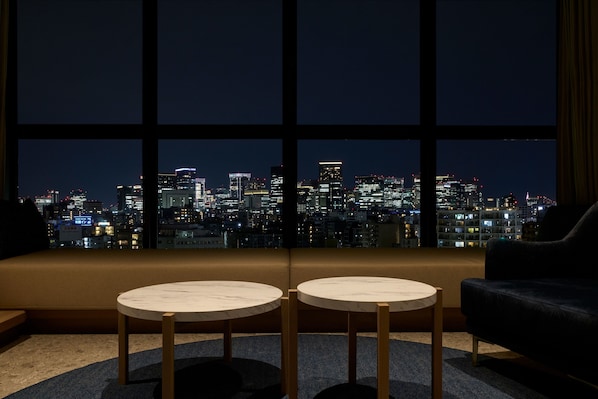 A room with a large window overlooking a cityscape at night. There are two round tables with wooden legs and a dark-colored sofa. - fav TOKYO RYOGOKU (Tokyo)