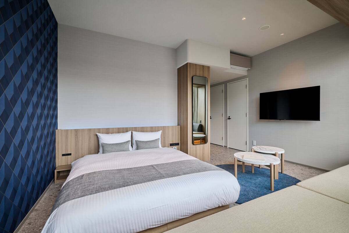 A modern hotel room with a large bed, a small desk, a television, and a mirror.