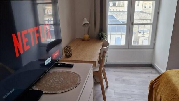 Une chambre d’hôtel dotée d’un grand téléviseur à écran plat affichant le logo de Netflix, d’un bureau en bois avec une lampe, d’une chaise et d’un lit recouvert d’une couverture marron.