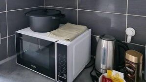 Une cuisine équipée d’un four à micro-ondes, d’une bouilloire et d’une machine à café. Des étagères situées au-dessus servent à ranger la vaisselle et les tasses.