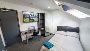 Habitación de hotel con cama, escritorio con una computadora portátil, televisión montada en la pared y tragaluz sobre la cama.