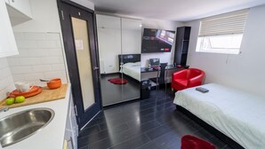 Et lille hotelværelse med tekøkken, seng, fjernsyn og en rød stol.