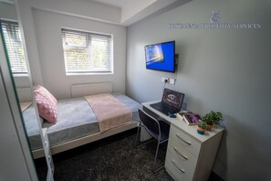 A bedroom with a bed, a desk, a laptop, a TV, and a radiator. - Lovely homely studio available (Birmingham)