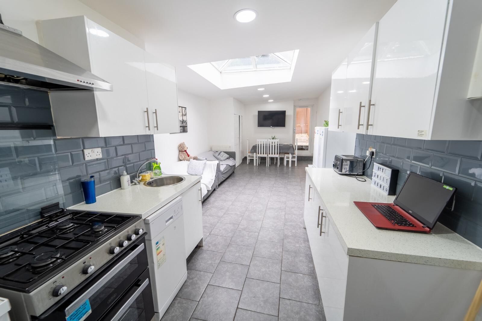 Une cuisine moderne équipée d’une cuisinière à gaz, d’un évier et d’un four à micro-ondes. On y trouve également un coin repas avec une table et des chaises, ainsi qu’un téléviseur fixé au mur.