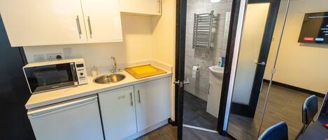 A modern kitchen with white cabinets, a microwave, a sink, and a wooden cutting board.
