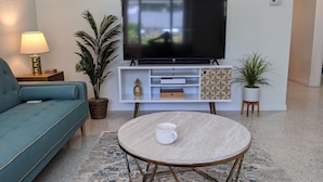 A living room with a teal sofa, a round coffee table, a TV on a white stand, and potted plants. - "Happy Ours" Gulfport - charming home, walk to beach and town (Gulfport)
