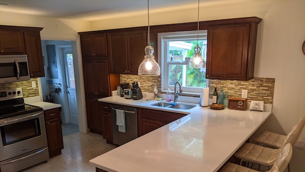 A kitchen with dark wooden cabinets, a stainless steel stove, a white countertop, a sink, and a window with a view of greenery outside. - "Happy Ours" Gulfport - charming home, walk to beach and town (Gulfport)