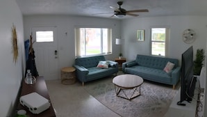 A living room with two blue sofas, a round coffee table, a ceiling fan, and a TV. - "Happy Ours" Gulfport - charming home, walk to beach and town (Gulfport)