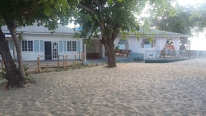Un bâtiment situé en bord de mer, doté d’une terrasse en bois, d’un espace salon couvert et d’une cour entourée d’une clôture.