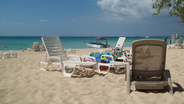 Une plage avec des chaises longues blanches et un bateau en arrière-plan.