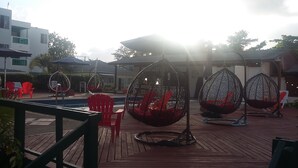 Un espace aménagé au bord de la piscine, avec des fauteuils suspendus en forme d’œuf et des chaises rouges.